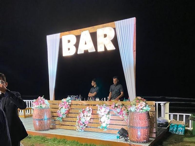 Outdoor 'BAR' counter — illuminated marquee-letter bar with DJ console and floral-dressed barrels at a night event — Arya Events Planner, Kharghar, Navi Mumbai