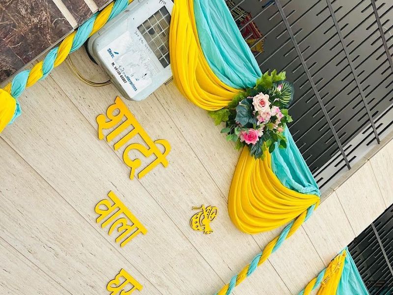 Welcome / entrance decor — yellow and teal pleated fans with floral bunches and a name board — Arya Events Planner, Kharghar, Navi Mumbai