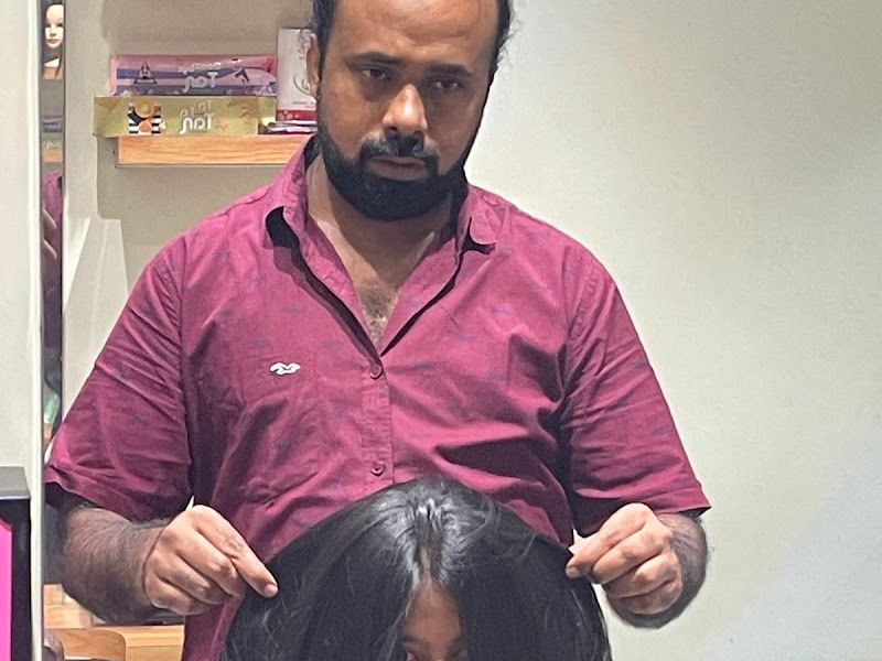 Male stylist in a maroon shirt blow-drying / styling a young client's long hair at the chair. — The Rush Family Salon, Airoli, Navi Mumbai