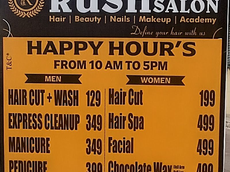 In-store 'Happy Hours' rate-card standee (L'Oréal branded) listing men's and women's pricing — haircut, cleanup, manicure, pedicure, hair spa, facial, wax, body massage — with phone numbers and the Airoli address. — The Rush Family Salon, Airoli, Navi Mumbai