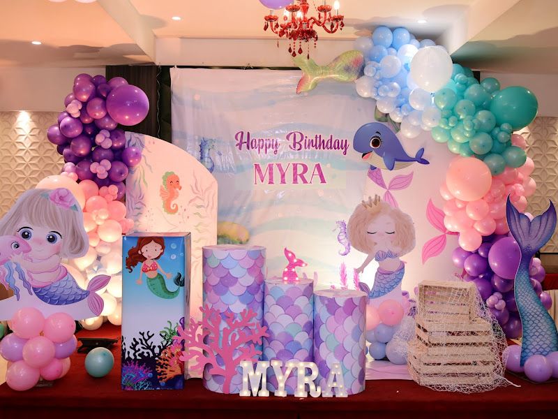 Mermaid-theme 1st birthday ('MYRA') — pastel pink, purple and blue balloon arch with mermaid and whale cutouts and a custom name backdrop — Arya Events Planner, Kharghar, Navi Mumbai