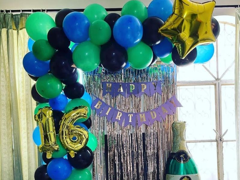 16th-birthday balloon decor — blue, green and black organic balloon garland with a foil number '16', fringe curtain and champagne-bottle foil — Arya Events Planner, Kharghar, Navi Mumbai