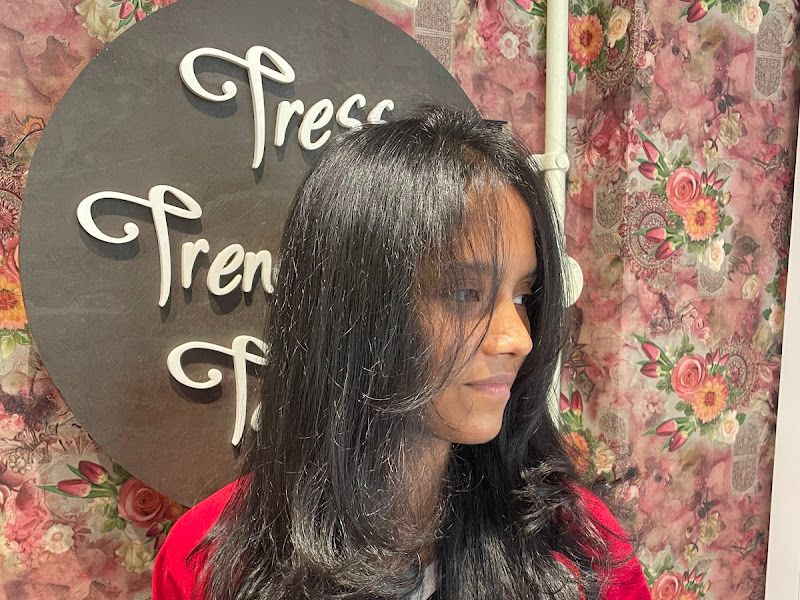 Long layered black hair styled against the floral 'Tress Trends' backdrop. — The Rush Family Salon, Airoli, Navi Mumbai