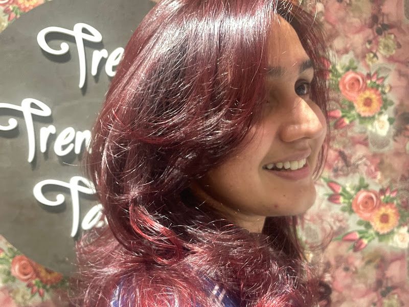 Vivid burgundy-red colour with layered curtain-bang styling, shot against the floral 'Tress Trends' wall. — The Rush Family Salon, Airoli, Navi Mumbai