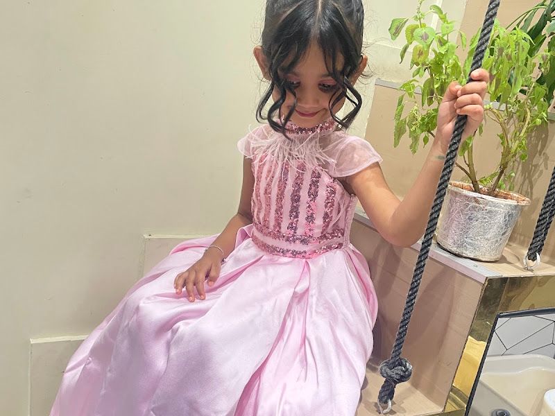 Cute decor detail — a child in a pink princess gown on the salon's hanging swing beside a potted plant; the swing is a recurring photo prop. — The Rush Family Salon, Airoli, Navi Mumbai