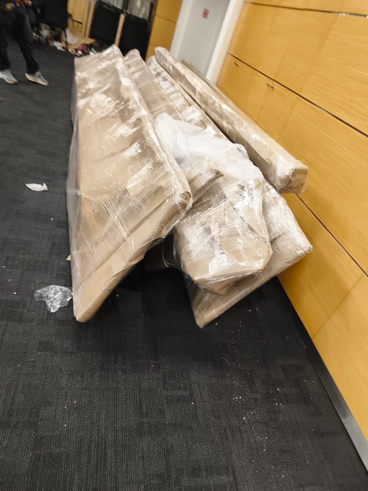 Plastic-wrapped furniture pieces stacked beside a wood-panelled wall