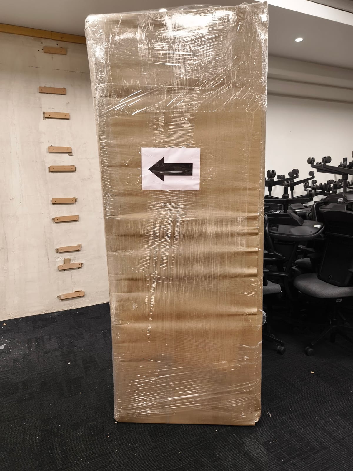 Wrapped cardboard pallet with a left-pointing arrow beside exercise equipment