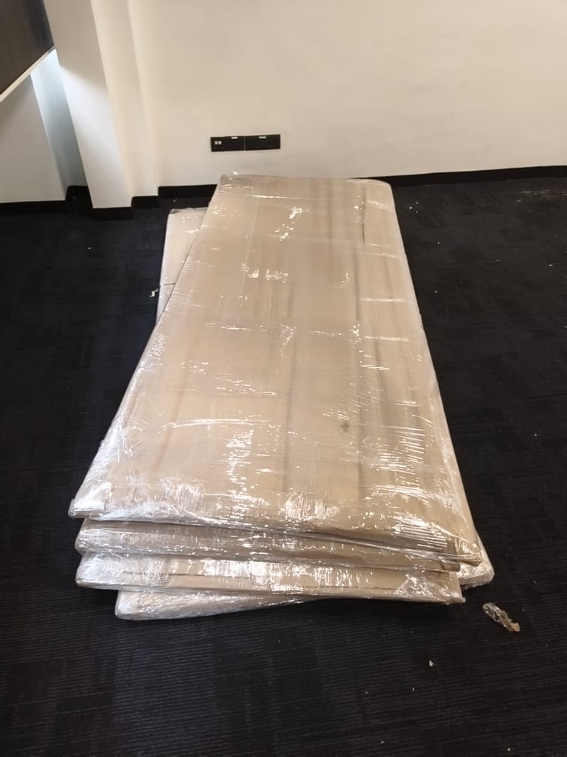 Stack of large flat plastic-wrapped packages on a dark carpeted floor