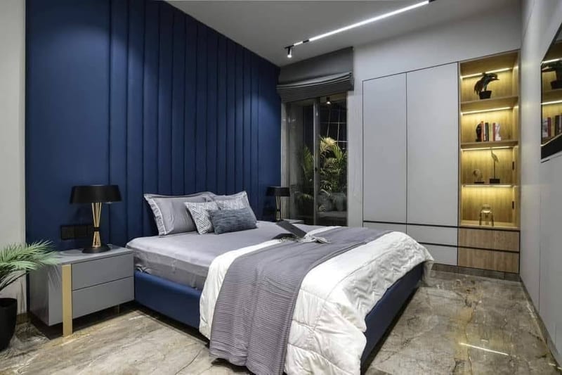 Bedroom with blue paneled accent wall, bed, bedside tables and illuminated shelving