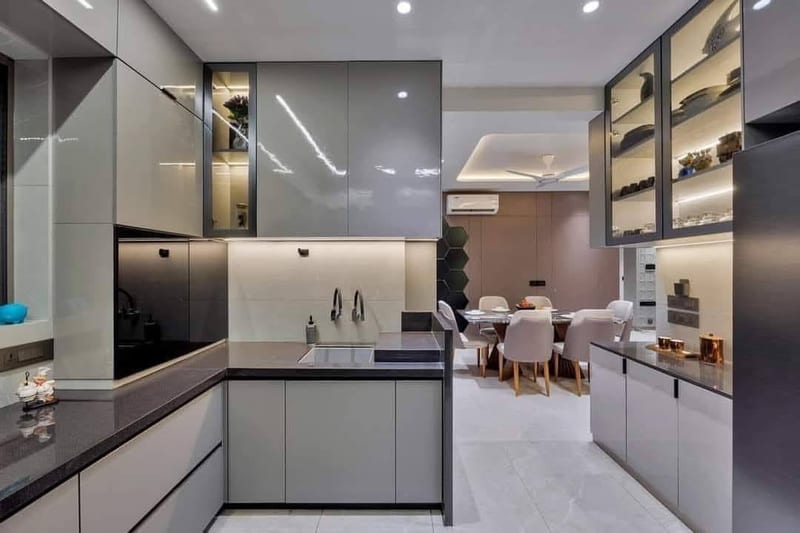 Modern kitchen with gray cabinets, island sink, dining table and illuminated display shelving